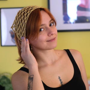 Pode incluir: Uma faixa de cabe&ccedil;a dourada com tecido aberto. A faixa de cabe&ccedil;a &eacute; feita de um material brilhante e &eacute; usada na cabe&ccedil;a. A pessoa na imagem est&aacute; usando uma regata preta.