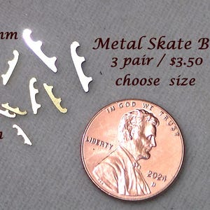 May include: Small metal skate blades in 5mm, 7mm, and 10mm sizes are displayed. The blades are silver and gold-colored, with a penny for size comparison. The text "Metal Skate Blades" and "choose size" are also visible.