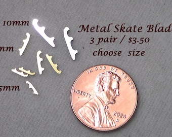 Puede incluir: Pequeñas cuchillas de patines de metal en tamaños de 5 mm, 7 mm y 10 mm. Las cuchillas son de color plateado y dorado, con una moneda para comparar el tamaño. El texto dice "Metal Skate Blades" y "choose size".