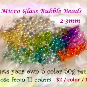May include: A collection of colorful micro glass bubble beads, 2-3mm in size, arranged in a vibrant display. The image features text that reads "Micro Glass Bubble Beads" and "Create your own 5 color 50g pack". The beads are available in 11 colors.