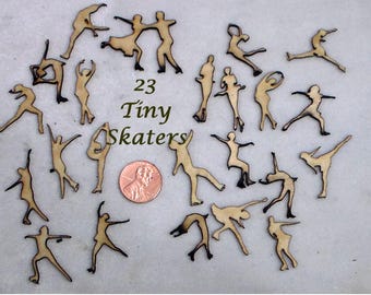 May include: Twenty-three tiny wooden skater figurines in various poses, some with dark edges. A penny is included for size reference. The text "23 Tiny Skaters" is also visible.