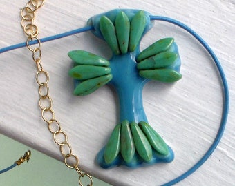 May include: A blue and green cross pendant necklace with a gold chain. The cross is made of blue glass with green glass accents.