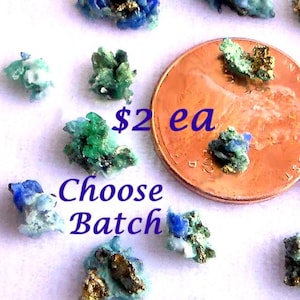 May include: Close-up of several small, colorful mineral specimens. The minerals display shades of blue, green, and gold, with a penny for size comparison. The text "Choose Batch" and "$2 ea" is visible.