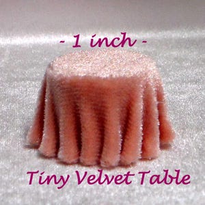 May include: A small, round velvet table in a peach hue. The table is about 2.5 cm in diameter and features a draped fabric design. The text "- 1 inch - Tiny Velvet Table" is written above and below the table.