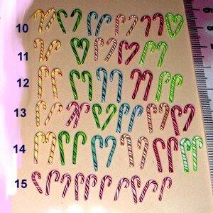 May include: Assortment of candy cane shaped charms in various colors and patterns, ranging in size from 9 to 15 millimeters. The charms are arranged in rows by size, with a ruler in the background for reference.