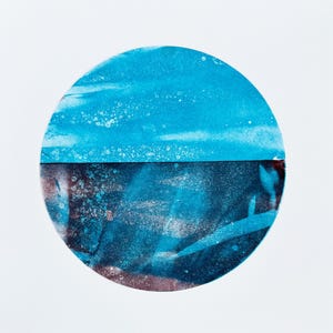 May include: Abstract art print featuring a circular design divided horizontally. The top half is a bright, textured turquoise, while the bottom half is a darker, mottled blue with hints of brown and white. The artwork is set against a white background.