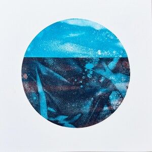 May include: Abstract art print featuring a circular design with a split composition. The top half is light blue, resembling a sky, while the bottom half is dark blue and brown, with textured patterns. The artwork is set against a white background.