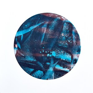 May include: Abstract art piece featuring a circular design with a white border. The artwork showcases a blend of dark blue, teal, and maroon hues, with a speckled effect and brushstroke-like patterns. The piece is set against a white background.