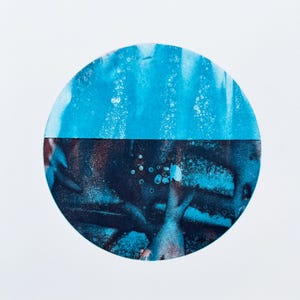May include: Abstract artwork featuring a circular design divided horizontally. The top half is a bright, textured blue, while the bottom half is a darker, mottled blue with hints of brown. The artwork is set against a white background.