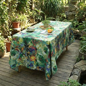 May include: A rectangular tablecloth with a vibrant floral pattern in shades of green, blue, yellow, and red. The tablecloth is draped over a wooden table, creating a colorful and decorative surface for outdoor dining or events.