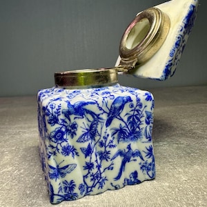 Peut inclure: Encrier en porcelaine bleu et blanc avec un couvercle à charnière. L'encrier présente un motif floral et d'oiseaux bleu détaillé. Le couvercle a un bord en métal argenté. L'encrier est rectangulaire avec un bord légèrement irrégulier.