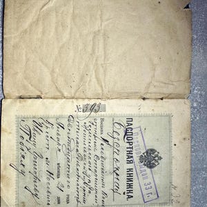 May include: An open, aged passport book with Cyrillic text and a stamped seal. The document is worn, with creases and discoloration, suggesting age. The text includes the words "Passport Book" and "Issued 33".