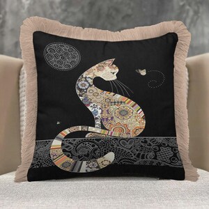 May include: A square throw pillow with a black background featuring a cat silhouette filled with intricate floral and geometric patterns. The cat sits on a decorative border, facing a small butterfly. The pillow has a beige fringed edge.