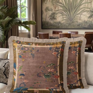 Può includere: Due cuscini decorativi con un design floreale. I cuscini presentano un centro malva con un motivo dettagliato di fiori e fogliame nei toni del blu, rosa e giallo. I cuscini hanno un bordo a balze e un bordo verde scuro.