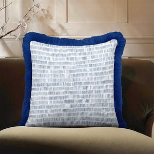 Könnte beinhalten: Quadratisches Zierkissen mit weißem Hintergrund und blauem vertikalen Strichmuster. Das Kissen hat einen dicken, gefransten, dunkelblauen Rand. Das Kissen liegt auf einem braunen Sofa.