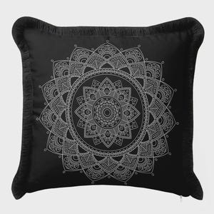 Op de afbeelding: Zwart vierkant kussen met een wit mandala-ontwerp. Het ingewikkelde patroon is gecentreerd op het kussen en wordt omgeven door een franjebies. Het is een decoratief item.