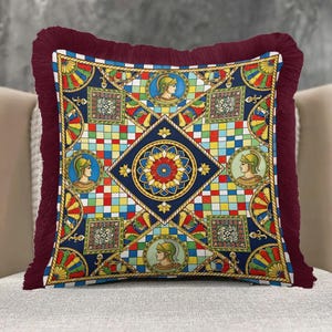 May include: Square decorative pillow with a colorful geometric pattern featuring portraits, floral designs, and a dark red fringe border. The pillow has a blue, yellow, red, and green color scheme.