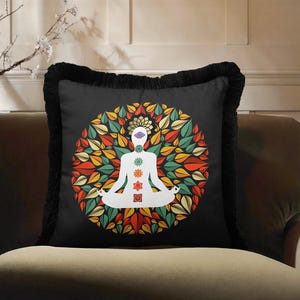 May include: Black square throw pillow with a white silhouette of a person in a yoga pose, surrounded by colorful leaves. The pillow has a black fringe border and is placed on a brown sofa.
