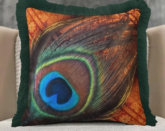 May include: Square decorative pillow featuring a close-up of a peacock feather design. The pillow has a dark green fringe border and a vibrant color palette of blue, brown, green, and orange. The pillow is placed on a neutral-colored surface.