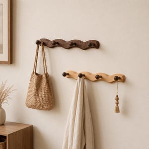 May include: Two wall-mounted wooden coat racks with a wavy, scalloped edge design. The top rack is dark brown wood with four pegs, holding a woven tan tote bag. The bottom rack is light wood with four dark brown pegs, holding a beige cloth.