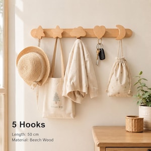 Peut inclure: Un porte-manteau mural en bois de hêtre de 50 cm de long avec cinq crochets en forme d'arbre, d'étoile, de nuage, de cœur et de lune. Il supporte un chapeau de paille, un sac en toile imprimé, un pull beige, des clés et une pochette à cordon.