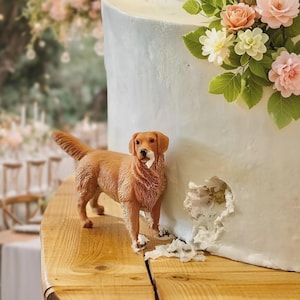 May include: A light blue frosted cake decorated with sugar flowers and a golden retriever figurine. The cake is on a wooden surface, with a bite taken out of the side. The cake is decorated with pink, white, and green sugar flowers.