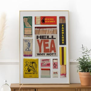 May include: A framed artwork featuring vintage matchbox designs with text like "HELL YEA WHY NOT?" and "NOT MY CIRCUS NOT MY MONKEYS." The artwork includes various colors and fonts, creating a retro aesthetic. The frame is gold.