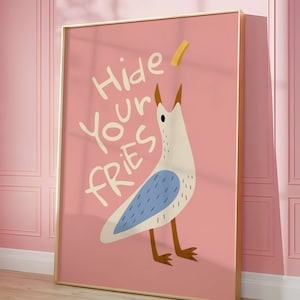 May include: A framed art print featuring a cartoon seagull with a blue wing design and brown legs, set against a pink background. The text "Hide Your Fries" is written in white. The frame is gold.