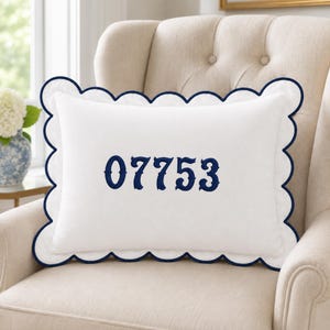 May include: A rectangular white throw pillow featuring a scalloped edge trimmed in navy blue. The center of the pillow displays the embroidered navy blue numbers 07753 in a decorative serif font. The pillow has a clean, crisp appearance.