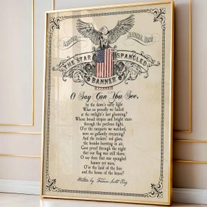 May include: A framed print featuring the lyrics to The Star-Spangled Banner, written by Francis Scott Key. The design includes a central illustration of an eagle perched atop an American flag, surrounded by ornate black scrollwork on a cream background.