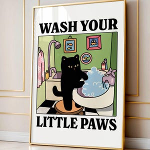 Peut inclure: Une affiche encadrée représentant un chat noir de dessin animé se lavant les pattes dans une baignoire. L'affiche porte l'inscription "WASH YOUR LITTLE PAWS" en lettres noires. La scène de la salle de bain comprend une douche, un évier et des tableaux décoratifs.