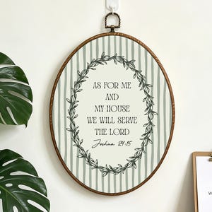 May include: Oval-shaped wall hanging with a wooden frame and a metal loop for hanging. The artwork features a cream-colored background with vertical green stripes. The text reads "AS FOR ME AND MY HOUSE WE WILL SERVE THE LORD Joshua 24:15" surrounded by a leafy wreath.