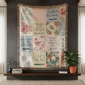 May include: A patchwork throw blanket with floral and plaid patterns in shades of pink, blue, and cream. The blanket features inspirational quotes from the Bible. The edges are fringed. The blanket is displayed on a dark gray wall.