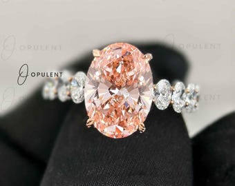 May include: A ring featuring a large oval-cut peach-coloured centre stone set in a metal band. The band is accented with smaller, clear oval-cut stones along the sides. The word OPULENT is visible in the background, repeated in a watermark pattern.