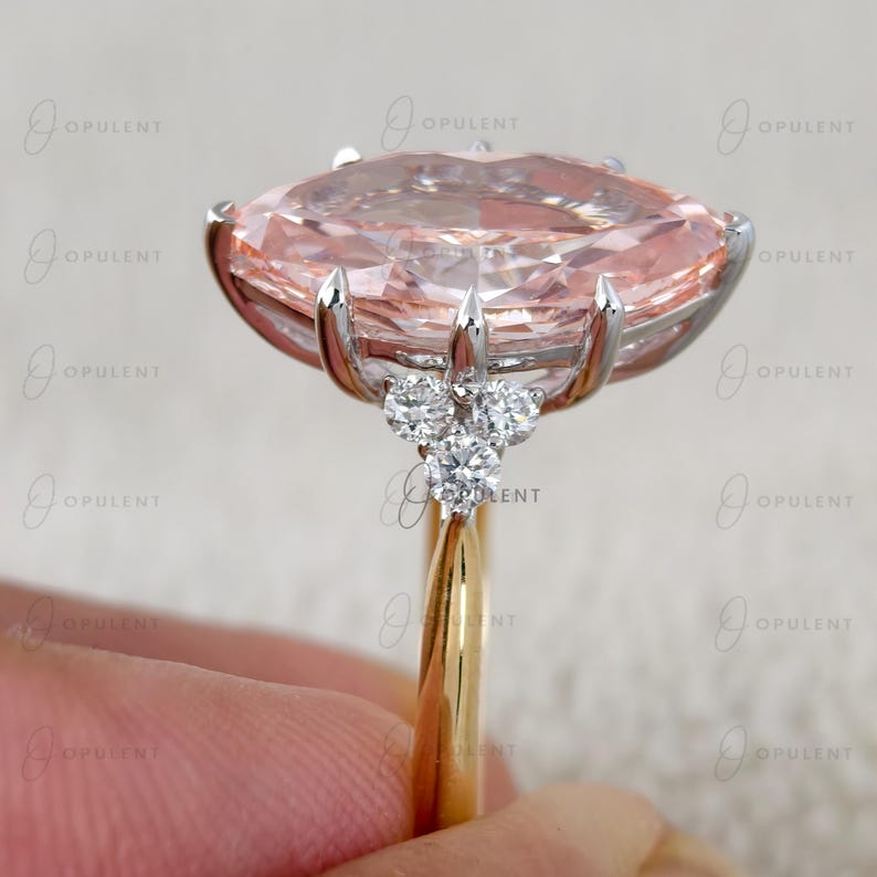 May include: A ring featuring a large, marquise-cut peach-coloured gemstone set in a silver-toned metal prong setting. The band is gold-toned, and the setting is accented with three small, round, clear white diamonds on each side of the centre stone.