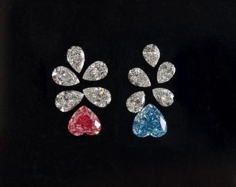 May include: Two clusters of faceted gemstones arranged in a fan shape. Each cluster features four clear pear-cut stones above a single heart-cut stone. One heart-cut stone is vibrant pink, while the other is a bright blue, set against a black background.