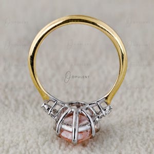 May include: A ring featuring a round, peach-coloured gemstone set in a silver-toned metal basket with small accent stones along the sides. The band of the ring is made of polished yellow gold, creating a two-tone design with a clear, circular profile.