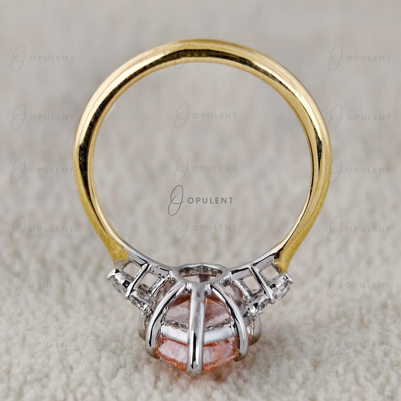 May include: A ring featuring a round, peach-coloured gemstone set in a silver-toned metal basket with small accent stones along the sides. The band of the ring is made of polished yellow gold, creating a two-tone design with a clear, circular profile.