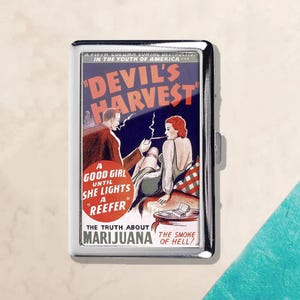 Puede incluir: Un estuche de cigarrillos plateado con un anuncio vintage de "Devil's Harvest". La obra de arte representa a un hombre y una mujer fumando, con el texto "A Good Girl Until She Lights a Reefer". El estuche tiene una superficie brillante y reflectante.