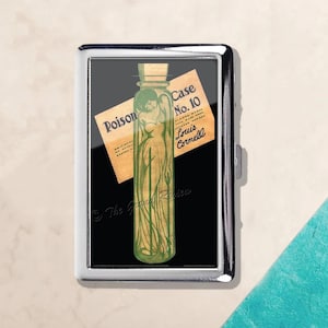 May include: A silver cigarette case featuring a vintage illustration. The artwork depicts a green bottle with a woman inside, and a label that reads "Poison Case No. 10 Louis Cornell". The background is black.