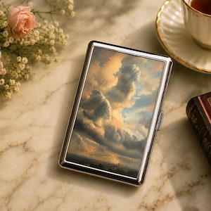 May include: A rectangular metal cigarette case featuring a glossy, high-resolution print of a dramatic, golden-hour sky filled with voluminous, textured clouds. The case has a polished silver-toned frame and a slim, hinged design for storage.