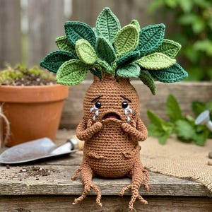 May include: A handmade crochet Mandrake plant doll with a distressed expression. The doll has a brown body, green leaves, and is crying. It is sitting on a wooden surface with gardening tools and potted plants in the background.