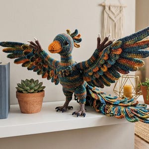 May include: A handcrafted crochet bird figure with wings spread wide, featuring a vibrant color palette of teal, orange, and brown yarn. The creature has a textured, multi-layered plumage, a prominent orange beak, and dark, clawed feet.