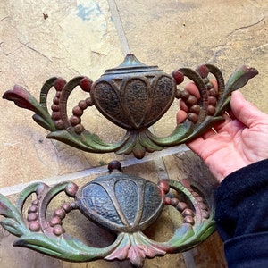 May include: Two antique cast iron decorative pieces with a green, red, and black paint finish. The pieces feature a stylized floral design with a central urn-shaped element.