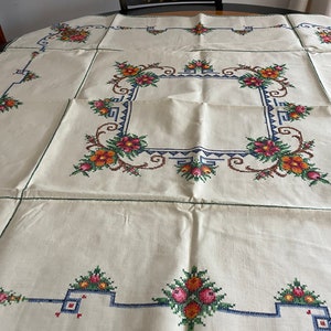 May include: White linen tablecloth with a green, blue, and orange embroidered floral border.