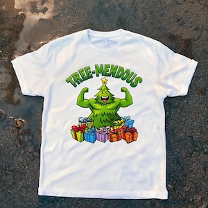 Könnte beinhalten: Weißes T-Shirt mit einem grünen Cartoon-Weihnachtsbaum, der seine Muskeln anspannt, umgeben von bunten Geschenkboxen. Der Text "TREE-MENDOUS" ist über dem Baum gewölbt. Ein lustiges, festliches Design für die Weihnachtszeit.