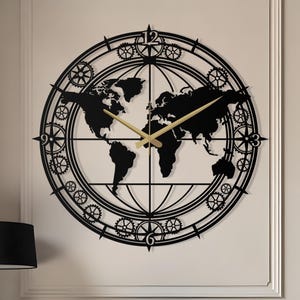 May include: A black metal wall clock featuring a world map design. The clock has gold-colored hands and a circular frame with gear-like details. The clock is mounted on a cream-colored wall above a white sofa with black pillows.