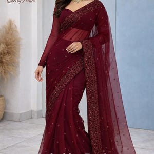Può includere: Sari bordeaux con intricati ricami e una sovrapposizione trasparente. La blusa a maniche lunghe e il bordo sono impreziositi da ricami dettagliati. Il testo "Label by Pavitra" è visibile.