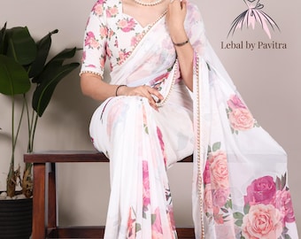 May include: White saree with a floral pattern in shades of pink and peach. The saree features a matching blouse with the same floral design. The border is trimmed with a delicate gold beaded edge. The text "Lebal by Pavitra" is visible.
