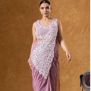 May include: A sleeveless, mauve formal dress with detailed white embellishments. The dress has a draped design and a decorative pattern down the front. The text "LABEL BY PAVITRA" is visible at the bottom of the image.